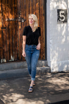 Female model in Gina v-neck black blouse tucked in jeans outdoor on a sunny day.