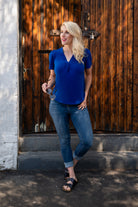 Female model in Gina v-neck blue blouse tucked in jeans outdoor on a sunny day.