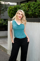 The female model wears a cowl neck top with no sleeves, the top is tucked into black pants. The print is small scale deep navy, white and teal geometric diamond shape pattern