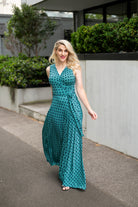 The female model wears a wrap dress in maxi length with no sleeves. The print is a small-scale deep navy, white and teal geometric diamond shape pattern. Front view