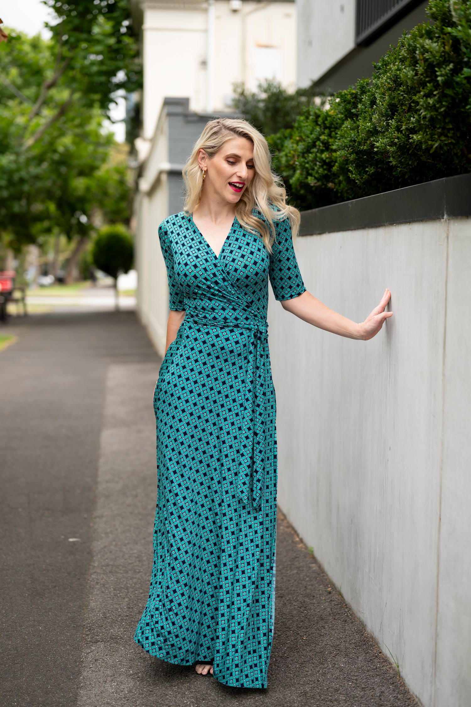  The female model wears a wrap dress in maxi length with 3/4 sleeves. The print is a small-scale deep navy, white and teal geometric diamond shape pattern. Front view